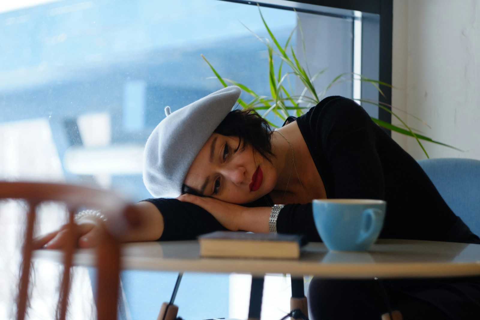Woman resting head on cafe table next to coffee cup